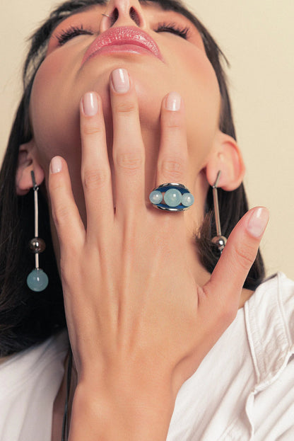 O Anel Sublime em Esmaltado Azul Anil e Ágata Azul Céu, com Banho de Ródio Negro, é uma peça sofisticada e moderna. A Ágata Azul Céu Liso harmoniza-se com o esmalte em tom azul anil, criando um visual elegante e marcante que se integra ao acabamento escuro do ródio.