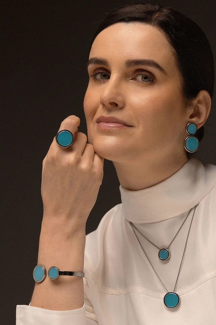 O Anel Único - Ágata Azul Céu, da Coleção Singular, une a serenidade das águas à sofisticação do acabamento escuro. A Ágata Azul Céu é reconhecida por promover calma, clareza mental e harmonia nas emoções, criando um contraste moderno e impactante com o metal escuro. Banhado a Ródio Negro, este anel de design imponente destaca a suavidade da pedra, sendo a peça ideal para mulheres que buscam um acessório contemporâneo que transmita paz interior com uma personalidade forte.